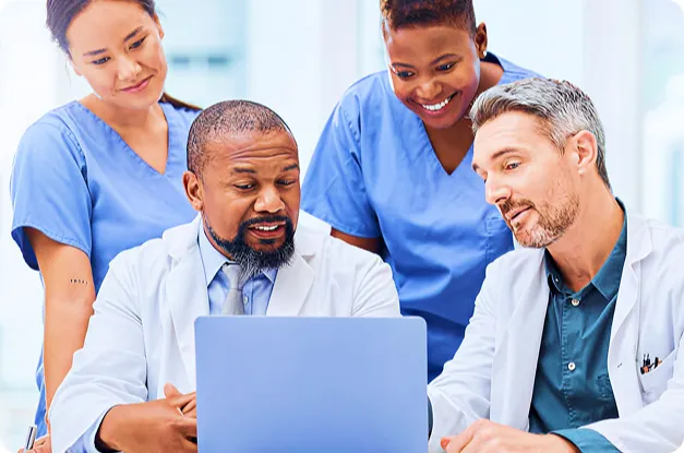 Group of four medical professionals collaborating while looking at a laptop screen