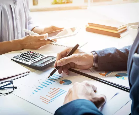 Close up of two people at a desk reviewing charts with a calculator