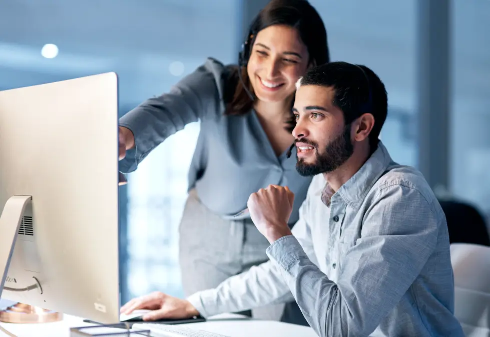 Two business professionals smile and talk while reviewing a computer screen