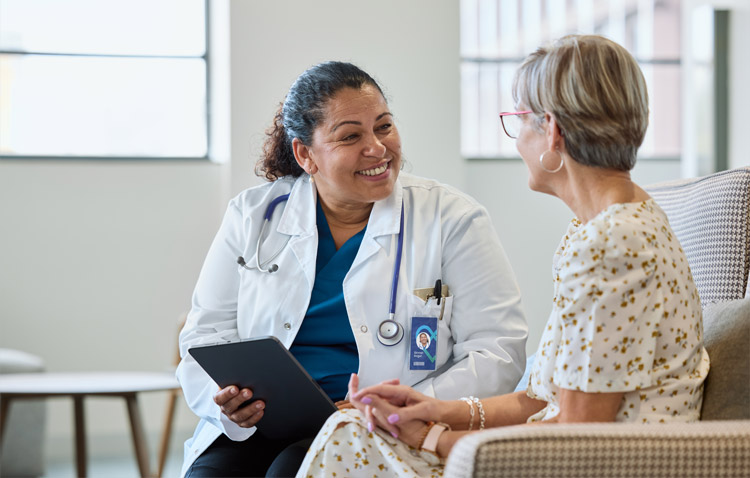 Physician holding a tablet while sitting with a patient and smiling