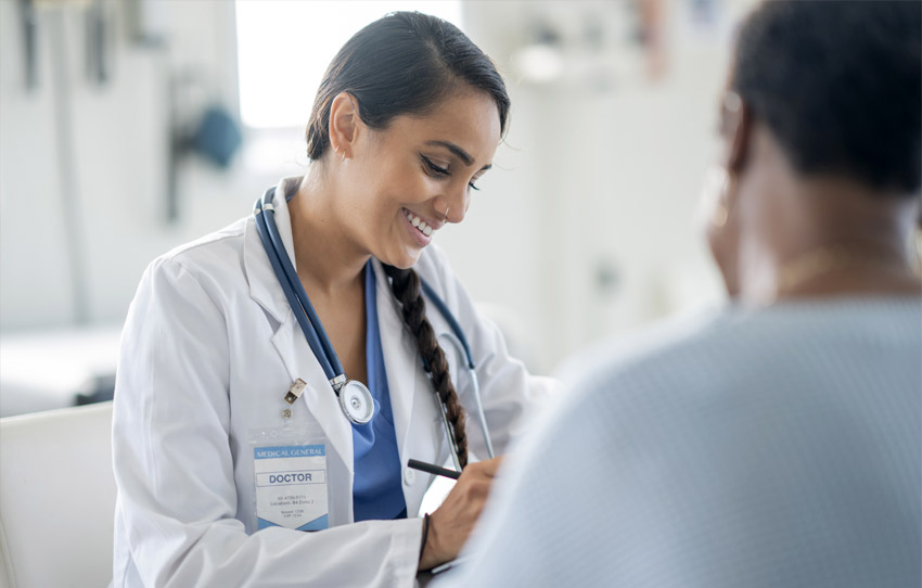Physician smiles while writing and speaking with patient