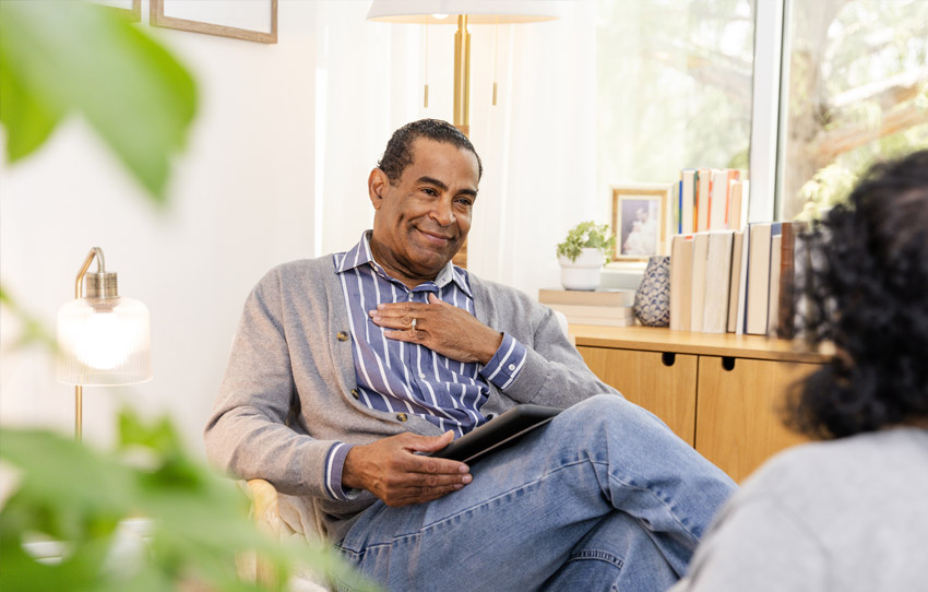 Professional holding tablet smiles while speaking with someone in a casual office setting