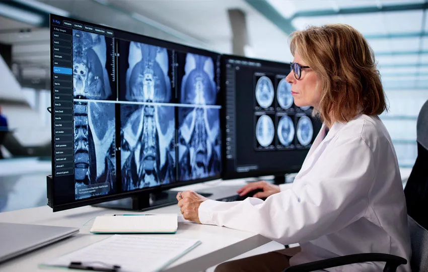 Medical professional reviews multiple body scans on multiple computer screens