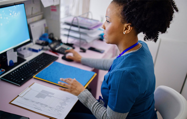 Medical professional reviewing a computer screen and paperwork at desk