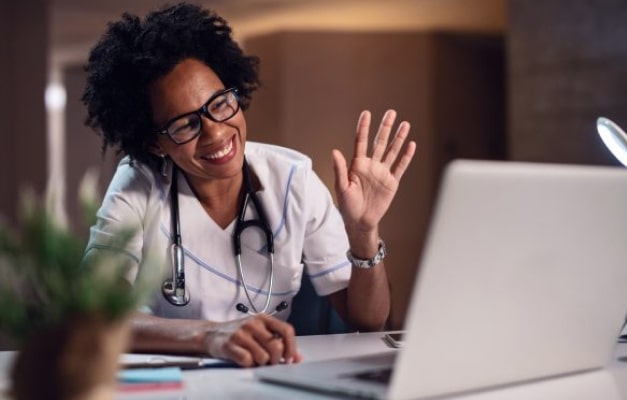 Medical professional waving to laptop screen at a desk