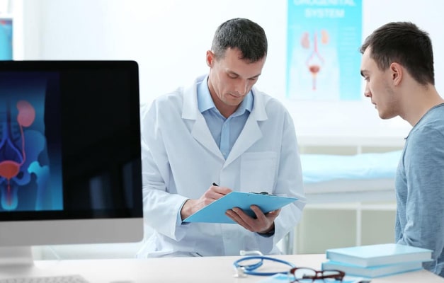 Physician writes in a folder with a patient and computer screen nearby