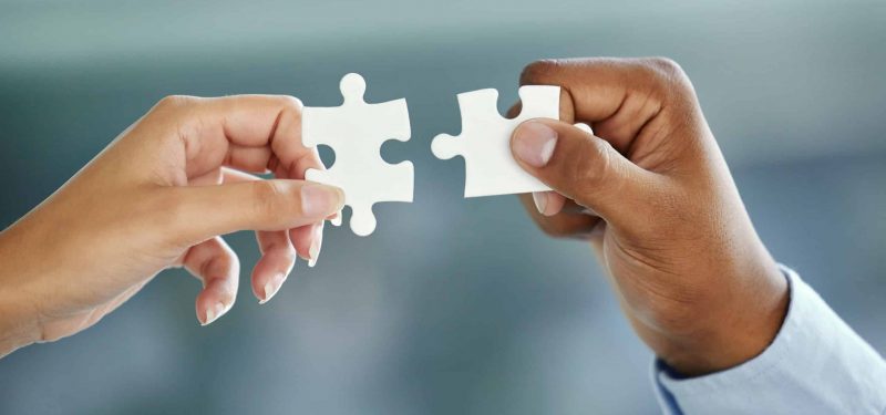 Cropped shot of two unrecognizable businesspeople fitting puzzle pieces together while standing in their office.